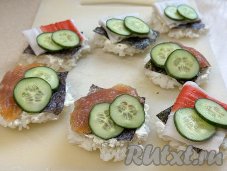 Поверх нори выложить кусочек тонко нарезанной слабосолёной красной рыбы или развёрнутую крабовую палочку. Огурец нарезать на тонкие кружочки. Выложить по 2 кружочка огурца на каждую суши-вафлю.