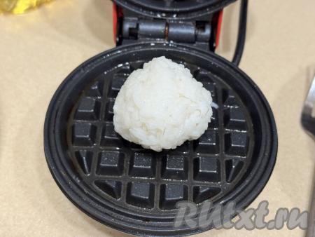 Как только рис остынет, влажными руками сформировать из него шарики весом по 40 грамм (у меня получились 7 шариков). Вафельницу разогреть, смазать створки вафельницы растительным маслом. Выложить шарик риса в вафельницу.