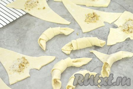 Начиная со стороны с ореховой начинкой, сворачиваем каждый треугольник из теста в рулетик. Кончик теста у свёрнутого рогалика должен быть снизу.