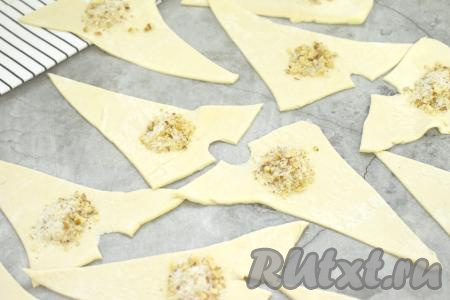 Углы у основания каждого треугольника из теста немного разводим в сторону. Отступив от краёв теста по 1 сантиметру, возле разреза выкладываем примерно половину чайной ложки смеси из грецких орехов и сахара.