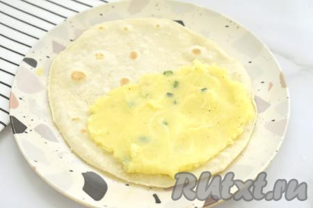 Горячую лепёшку со сковороды перекладываем на плоскую тарелку. На одну сторону лепёшки, немного отступая от краёв, равномерно выкладываем примерно 1,5 столовых ложки картофельно-сырной начинки.