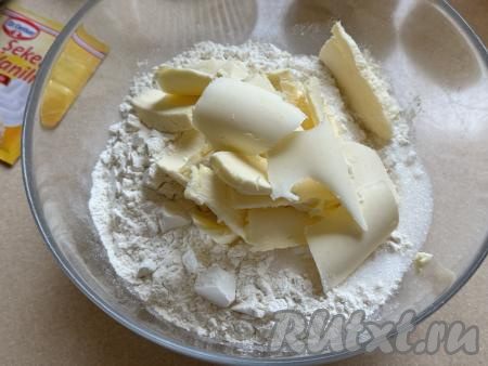 Сливочное масло достать из холодильника, сразу нарезать его на небольшие кусочки и добавить в миску с мукой.
