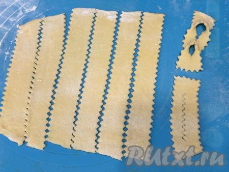 Нарезать каждый раскатанный пласт теста на полоски шириной примерно 3 сантиметра (для того чтобы полоски смотрелись более симпатично, я нарезала фигурным ножом). Разрезать полоски на части длиной примерно 10 сантиметров. Получатся заготовки хвороста размером 3 сантиметра на 10 сантиметров. Сделать по середине каждой заготовки разрез, вывернуть 1 раз через этот разрез одну сторону заготовки. 