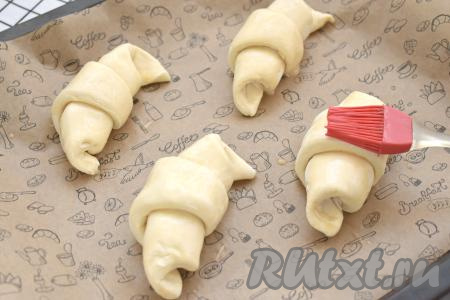 Круассаны на небольшом расстоянии друг от друга (круассаны увеличиваются в процессе выпечки) выкладываем на противень, застеленный бумагой для выпечки. Оставляем круассаны на 20 минут при комнатной температуре, чтобы слоёное дрожжевое тесто немного подошло. Затем в кружке взбиваем сырое яйцо и смазываем им круассаны.