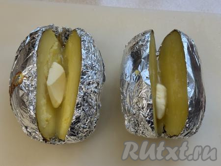 Готовую картошку прямо в фольге аккуратно переложить на разделочную доску. Разрезать картошину вдоль на две части, не дорезая до конца. Выложить внутрь картошки по кусочку сливочного масла.