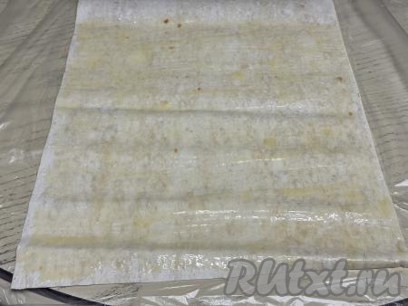 Сливочное масло растопить, дать ему немного остыть. На столе расстелить лист лаваша, смазать его растопленным маслом. 