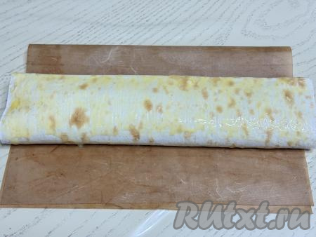 Сформированный рулет с тыквой выложить на противень, застеленный ковриком (или бумагой) для выпечки. В небольшой ёмкости яичный желток взбить вилкой до однородности, а затем получившейся смесью смазать поверхность рулета из лаваша. 