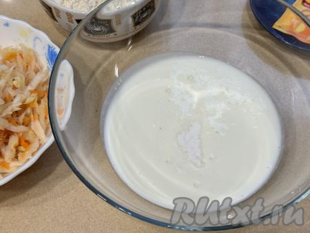 Прежде всего замесим бездрожжевое тесто для жареных пирожков, для этого в глубокую миску нужно влить кефир, всыпать соду, перемешать и оставить минут на 5. За это время сода полностью погасится в кефире, на поверхности смеси появятся пузырьки. Смесь кефира и соды немного увеличится в объёме.