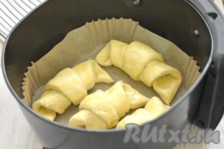 В небольшой ёмкости (например, в стакане) взбиваем вилкой яичный желток до однородности. Смазываем круассаны желтком и выкладываем в чашу аэрогриля, предварительно застеленную пергаментом.