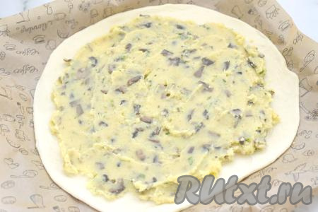 Поднявшееся дрожжевое тесто обминаем, делим на 2 равных части. Одну часть теста на присыпанной мукой поверхности раскатываем в круглую лепёшку ориентировочно диаметром 29 сантиметров, перекладываем на противень, застеленный пергаментом. На лепёшку, отступая от краёв теста по 2 сантиметра, равномерно выкладываем начинку из картошки и грибов.