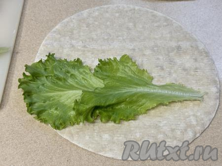 Теперь можно приступать к формированию цезарь-ролла. Мы будем формировать 4 ролла, поэтому и продукты для начинки нужно делить на 4 части. Ближе к центру круглого лаваша нужно выложить 2 листа зелёного салата, как на фото.