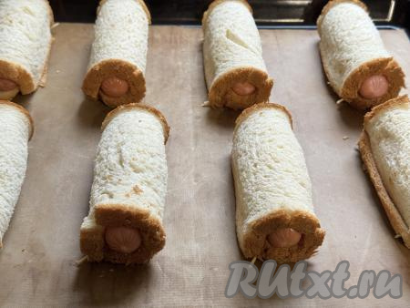 Завернуть сосиску в хлеб, скрепить край зубочисткой. Аналогично сформировать остальные сосиски в тостовом хлебе. Выложить заготовки на противень, застеленный ковриком (или пергаментом) для выпечки.