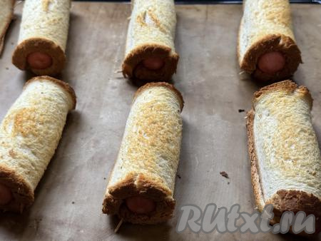 Запекать сосиски в хлебе в разогретой до 200 градусов духовке минут 10.