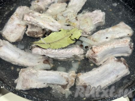 Влить в сковороду 550 миллилитров воды, добавить лавровый лист и горошины чёрного перца. Дать воде закипеть на сильном огне, уменьшить огонь до минимума, накрыть сковороду крышкой, томить рёбрышки 40 минут. Пока тушатся рёбрышки, нужно будет подготовить гречку. Для этого блюда я взяла 210 грамм гречки - это 1 стакан объёмом 250 миллилитров. Гречку, если необходимо, перебрать, удаляя порченые зёрнышки. Гречку выложить в сито, тщательно промыть проточной водой, оставить, чтобы стекла вода, на время, пока готовится мясо.