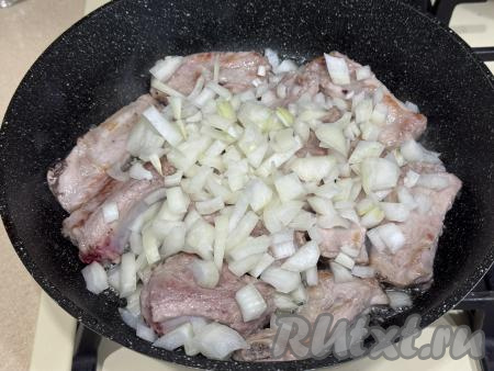 К обжаренным рёбрышкам добавить очищенный и мелко нарезанный лук, аккуратно перемешать. 