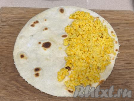 Горячую лепёшку переложить со сковороды на доску. Отступив от краёв одной половины лепёшки по 1-1,5 сантиметра, равномерно выложить 2 столовых ложки каши. 