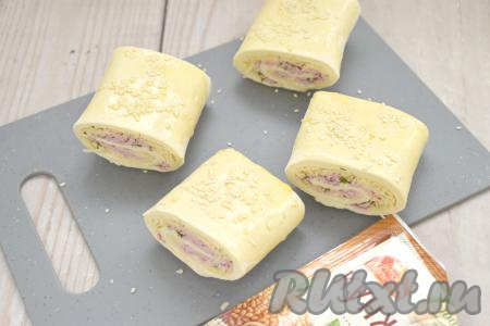 В стакане вилкой взбиваем яичный желток до получения однородной массы. Слойки переворачиваем "швом" вниз, смазываем их взбитым желтком и посыпаем сверху кунжутом.