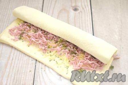 Начиная с широкой стороны пласта, сворачиваем тесто с начинкой в рулет.