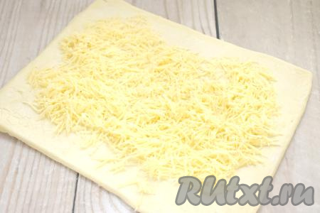 Сыр натираем на крупной тёрке. Отступая от краёв раскатанного теста по 1,5-2 сантиметра, посыпаем тесто натёртым сыром.