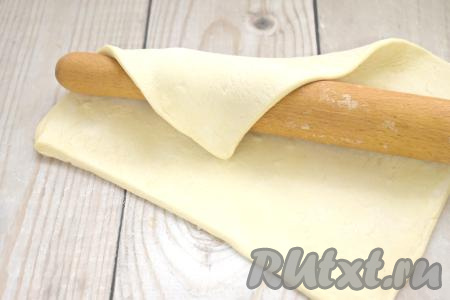 Слоёное тесто можно взять как дрожжевое, так и бездрожжевое (в этот раз я купила слоёное дрожжевое тесто). Пласт слоёного теста размораживаем при комнатной температуре. Выкладываем разморозившееся тесто на припорошенный мукой стол и раскатываем скалкой в одном направлении до получения пласта теста размером 21 сантиметр на 26 сантиметров (примерная толщина раскатанного теста 3-4 миллиметра).