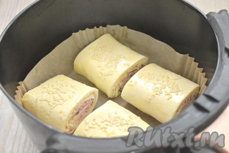 Застилаем чашу аэрогриля специальным вкладышем из пергамента (или вырезаем бумагу для выпечки по размеру чаши), выкладываем слойки с колбасой и сыром швом вниз.