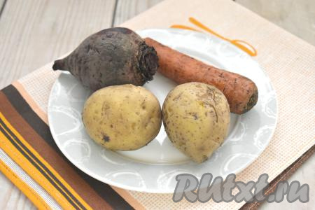 Картошку, свеклу и морковь тщательно моем, готовить их будем, не очищая от кожуры. В одну кастрюлю выкладываем картошку с морковью, заливаем полностью водой, ставим на огонь, после закипания варим на небольшом огне до готовности (на варку морковки обычно требуется минут 25-30, картофеля - минут 25, готовые овощи будут легко прокалываться ножом). В отдельной кастрюле отвариваем свеклу в кожуре до готовности (на варку свеклы с момента закипания воды потребуется 45-60 минут, продолжительность отваривания зависит от величины и сорта свеклы, как только корнеплод будет легко прокалываться ножом, значит он готов). Варёные овощи выкладываем на тарелку, даём остыть.