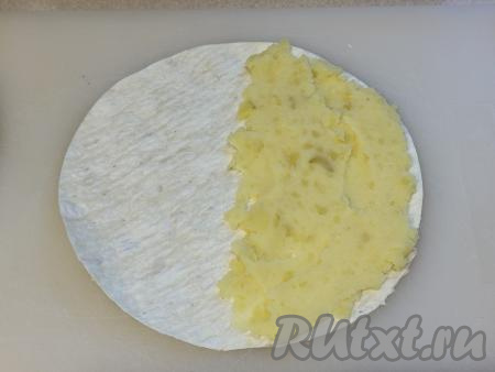 Немного отступив от краёв лаваша, на одну половину круга из лаваша выложить 2 столовых ложки картофельной начинки. Разровнять картошку, равномерно распределяя по половине лаваша, немного отступая от краёв. 