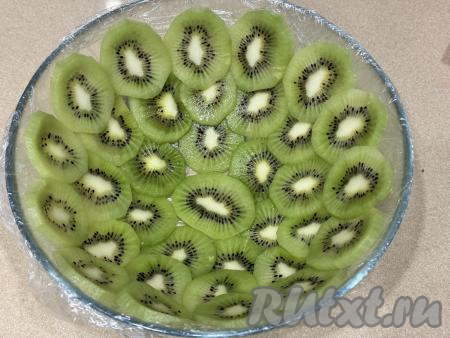 Взять миску (я взяла миску диаметром 20 сантиметров), выстелить её дно и бока пищевой плёнкой так, чтобы края плёнки свисали с краёв миски. Киви почистить и нарезать на достаточно тонкие кружочки. Дно и бока миски выложить кружочками киви, выкладывая киви немного внахлёст. 