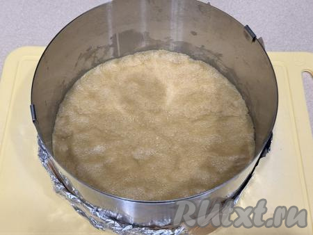 Взять разъёмную форму диаметром 18 сантиметров (в качестве формы я использовала разъёмное кулинарное кольцо, сделав дно из пергаментной бумаги и фольги, сложенной в несколько слоёв). В разъёмную форму выложить смесь из печенья и масла, разровнять, утрамбовать, формируя основу чизкейка. Поставить форму с основой чизкейка в холодильник на время, пока будем заниматься творожной начинкой. 