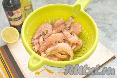 Для запекания я взяла замороженные варёно-мороженые королевские креветки. Выкладываем замороженные креветки в дуршлаг, ополаскиваем их холодной водой и оставляем их размораживаться при комнатной температуре, не забыв поставить под дуршлаг ёмкость, в которую будет стекать вода с креветок в процессе размораживания.