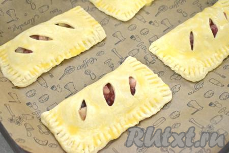 Постепенно сформировать все слойки и выложить их на противень, застеленный пергаментом (или листом для выпечки). В небольшой ёмкости взбить вилкой яичный желток до однородности. С помощью силиконовой кисточки смазать поверхность каждой слойки взбитым желтком.