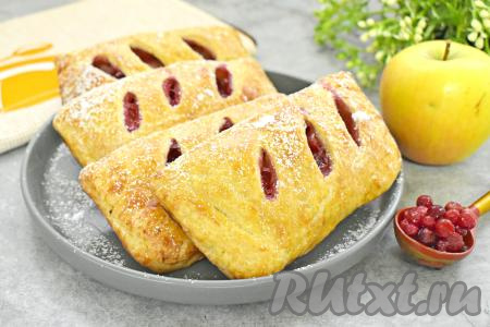 Готовую выпечку достать из духовки, дать слегка остыть, по желанию, присыпать сверху сахарной пудрой. Воздушное слоёное тесто отлично сочетается с сочной, аппетитной начинкой из яблок и брусники, поэтому слойки получаются очень вкусными. 