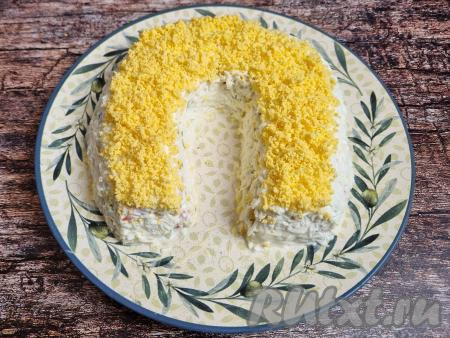 Отложенные ранее яичные желтки натереть на мелкой тёрке и разместить верхним слоем подковы, как на фото.