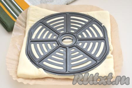 Заранее размораживаем слоёное дрожжевое (или бездрожжевое) тесто при комнатной температуре. Отрезаем кусок пергаментной бумаги, которым будем застилать дно и бока чаши аэрогриля. На бумагу выкладываем размороженное слоёное тесто. Поверх теста прикладываем решётку аэрогриля (диаметр решётки моего аэрогриля 16 сантиметров, именно пиццу такого диаметра мы и будем выпекать), вырезаем основу для пиццы. Тесто я не раскатывала, потому что размер решётки аэрогриля был немного меньше размера слоёного теста. Если размер решётки вашего аэрогриля больше размера пласта теста, тогда раскатайте размороженное слоёное тесто до нужного размера.