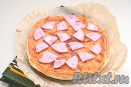 ​​​​​​​​​​​​​​​​​​​​На смазанную основу для пиццы выкладываем колбасу (или ветчину), нарезанную на небольшие кусочки.