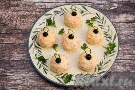 Поверх каждого крабово-сырного шарика разместить "крепление" из половины маслины и веточки петрушки, формируя ёлочные шарики.