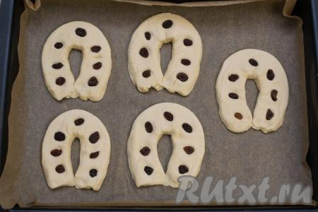 На каждую подковку разложить изюм, имитируя дырочки на подкове лошади. Изюм прижать сверху, чтобы он немного вдавился в тесто.&nbsp;Скрепить между собой концы каждой подковки, чтобы зафиксировать форму подковы.