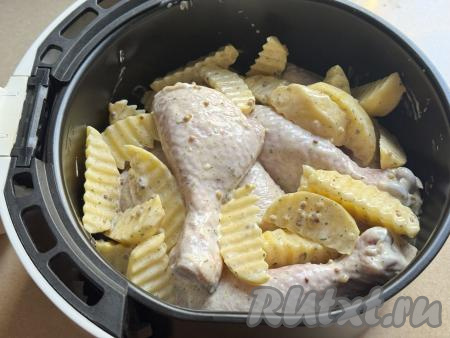 Из чаши аэрогриля убрать решётку. Выложить в чашу аэрогриля дольки картошки с куриными ножками.