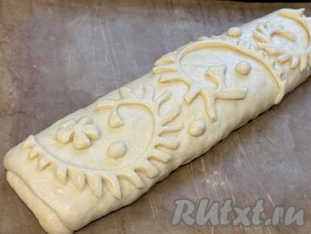 Перевернуть рулет швом вниз&nbsp;и переложить на противень, застеленный ковриком (или пергаментом) для выпечки. Оставить рулет на 15 минут под полотенцем. Из теста сформировать узоры для украшения и выложить поверх рулета.