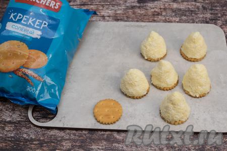 Руками, смоченными водой, вначале из одной части массы руками сформировать конус (лепится масса очень легко), сразу поставить конус на солёный крекер (сладкие крекеры для этой закуски не подойдут). Аналогично сформировать все конусы и поставить их на крекеры. Всего у меня получились 7 заготовок ёлочек на крекерах.