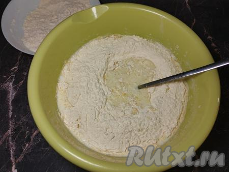 Частями начать добавлять в миску муку, каждый раз хорошо вмешивая её. Сначала перемешивать тесто ложкой, а когда оно начнёт собираться в шар, продолжать замешивать его руками, всыпая муку только по мере необходимости. Как только тесто станет мягким, не липнущим к рукам, больше добавлять муку не нужно.