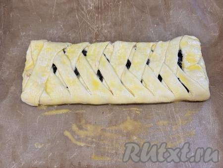 Переложить получившийся слоёный пирог с черносливом на противень, застеленный ковриком (или пергаментом) для выпечки. В небольшой ёмкости взбить вилкой яичный желток. Смазать поверхность пирога взбитым желтком.&nbsp;