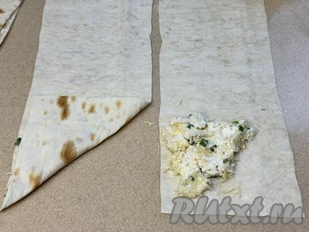 Лаваш нарезать на 8 полосок шириной ориентировочно 10 сантиметров. Ближе к одному узкому краю лаваша, немного отступая от краёв, выложить в виде треугольника&nbsp;1 столовую ложку начинки из зелени, сыра и творога, как на фото, затем подвернуть чистую часть узкой стороны лаваша на начинку по диагонали.