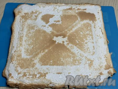Противень с готовым меренговым коржом достать из духовки. Корж вместе с ковриком (или пергаментом) переложить с противня на стол, оставить остывать, а затем перевернуть на силиконовый коврик (или на новый лист пергамента).