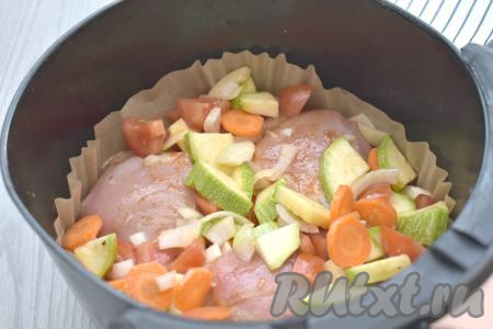 Чашу аэрогриля застилаем пергаментом, выкладываем куриные бёдра с овощами. Отправляем чашу в аэрогриль. Включаем аэрогриль, выставив температуру на 200 градусов, а время - на 40 минут.