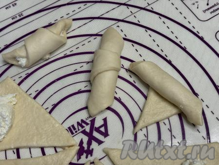 Начиная со стороны с творожной начинкой, свернуть треугольную заготовку из дрожжевого теста в рогалик.