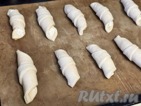 На противень, застеленный ковриком (или пергаментом) для выпечки, выложить заготовки дрожжевых рогаликов с творогом на расстоянии друг от друга. 