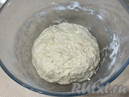 В общей сложности вымешивать тесто руками нужно не менее 7 минут. Частями добавляя муку и вмешивая её, замесить мягкое, пластичное тесто, которое практически не липнет к рукам. Муки может потребоваться как немного больше, так и немного меньше, чем указано в ингредиентах, главное - не забывать учитывать консистенцию замешиваемого теста. Миску с замешанным тестом накрыть пищевой плёнкой (или полотенцем) и поставить в тёплое место примерно на 1 час (до увеличения теста в объёме раза в 2-3).