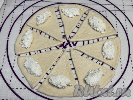 Ближе к широкому краю каждой треугольной заготовки из теста выложить по 1 чайной ложке творожной начинки.