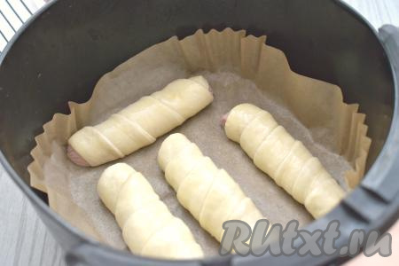 Затем в чашу аэрогриля, застеленную пергаментом,&nbsp;выкладываем сосиски, завёрнутые в дрожжевое тесто,&nbsp;на расстоянии друг от друга&nbsp;(тесто увеличится в объёме в процессе выпечки, поэтому не нужно выкладывать сосиски близки друг к другу).&nbsp;У меня помещаются в чашу аэрогриля 4 сосиски в тесте.&nbsp;В небольшой ёмкости взбиваем вилкой до однородности яйцо. Смазываем сосиски взбитым яйцом. Отправляем чашу в аэрогриль.&nbsp;